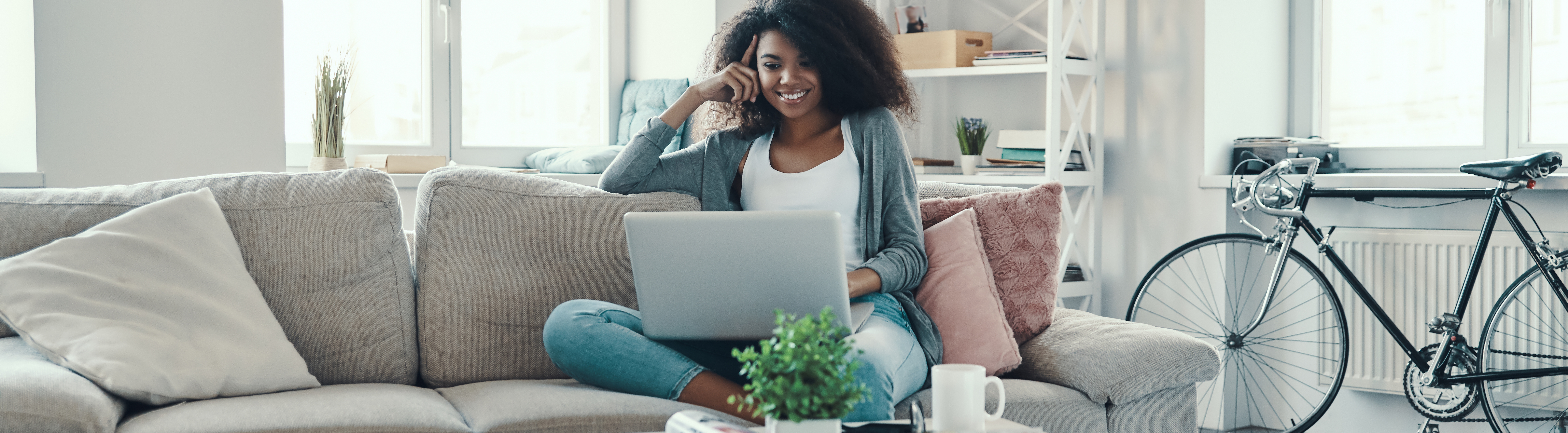 A young woman is using her laptop while at home Top horizontal, narrow-cropped photo banner of a young black woman in casual clothing using laptop while resting at home