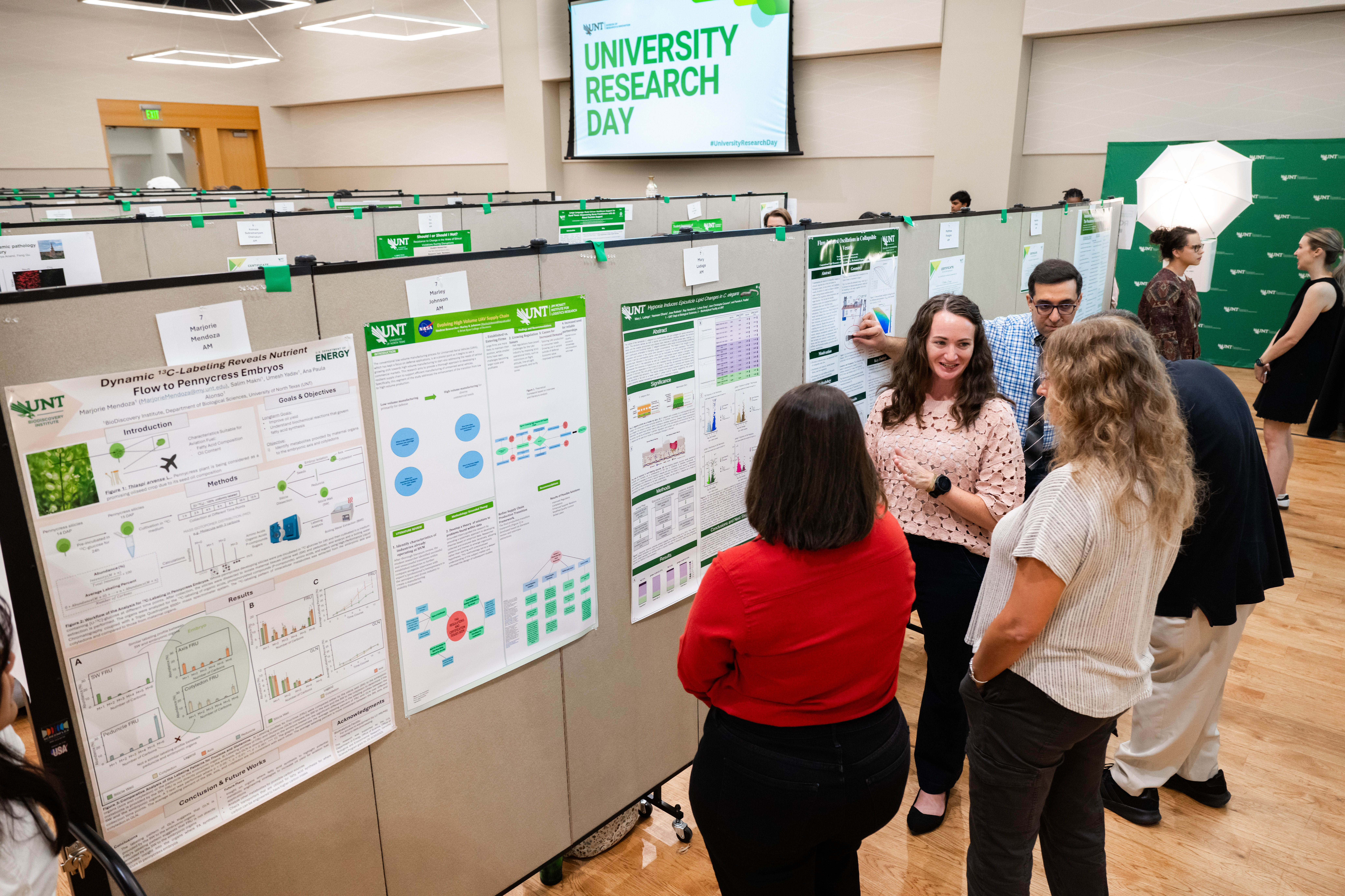 Photo of students presenting their research posters to attendees at the UNT University Research Day in a large indoor hall.
