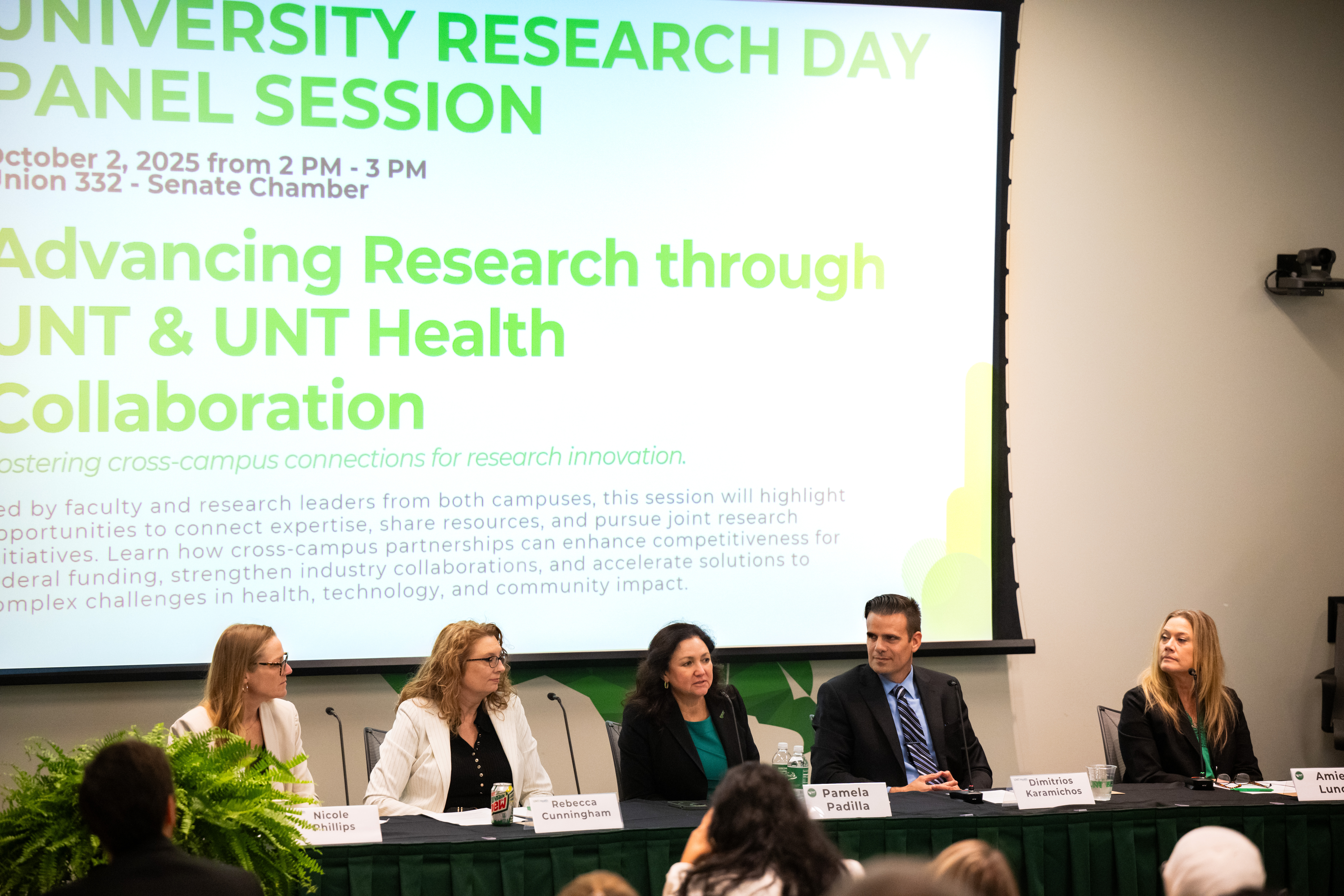 Photo of UNT Vice President of Research and Innovation Pamela Padilla (center) spoke at the afternoon panel. There is a super large digital screen with University Research Day Panel Session information on the wall behind them.