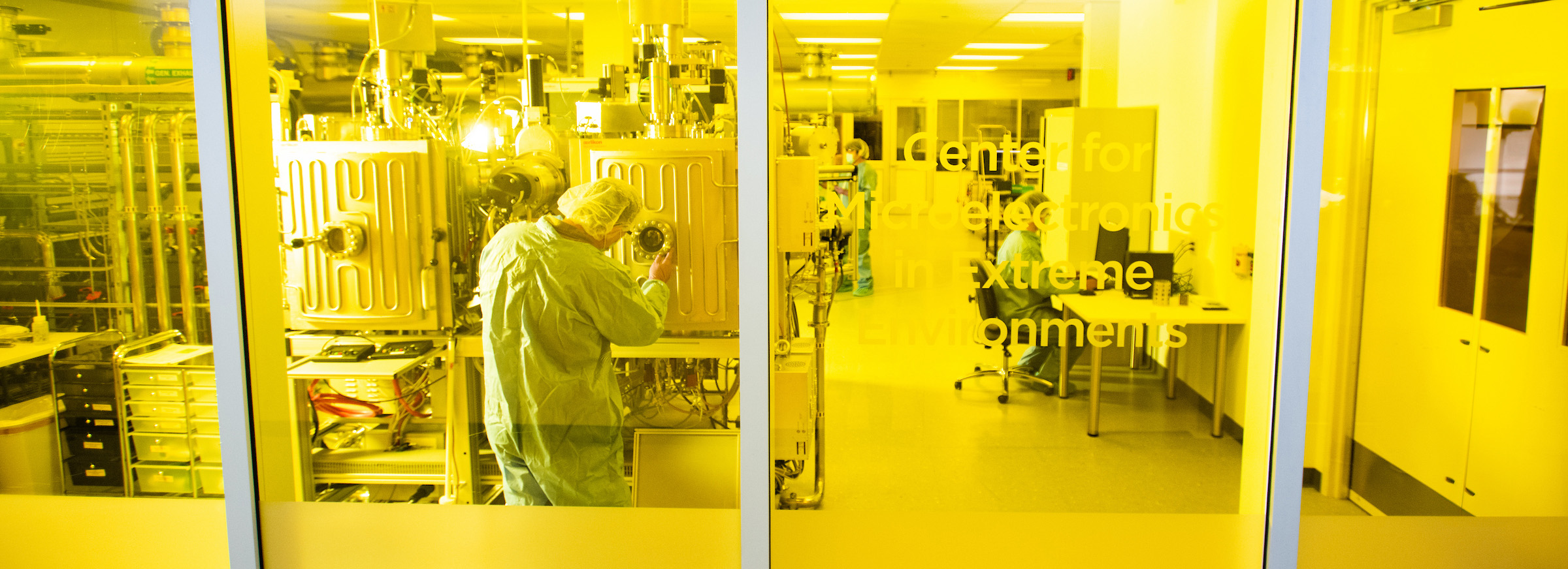 Full photo of researcher in cleanroom attire works inside the UNT Center for Microelectronics in Extreme Environments semiconductor laboratory at Discovery Park.