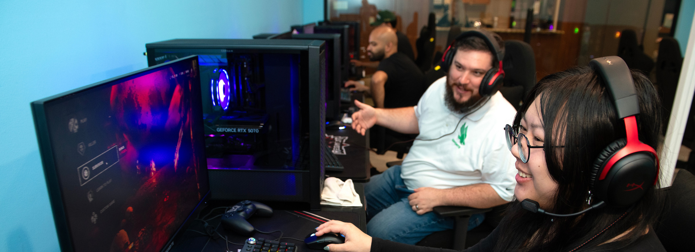 Photo of Dylan Wray, assistant director of UNT’s Esports program is sitting at a console with other visitors playing their own video game's. 