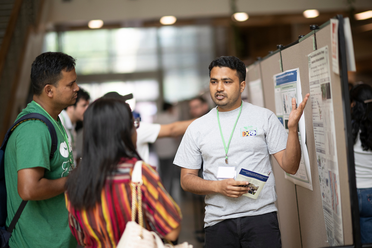 At the UNT expo, a photo of a student researcher talking with interested visitors and sharing their work 