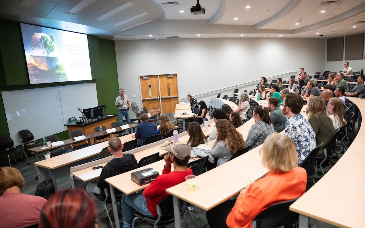 Photo of UNT's Richard Dixon giving his keynote address with a projected presentation to an audience in a classroom lecture hall