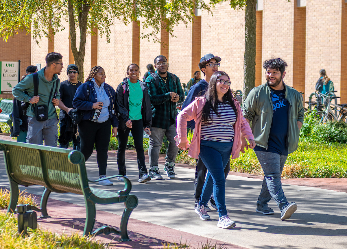 A full photo of a group of students walking together on a sunny UNT campus walkway.