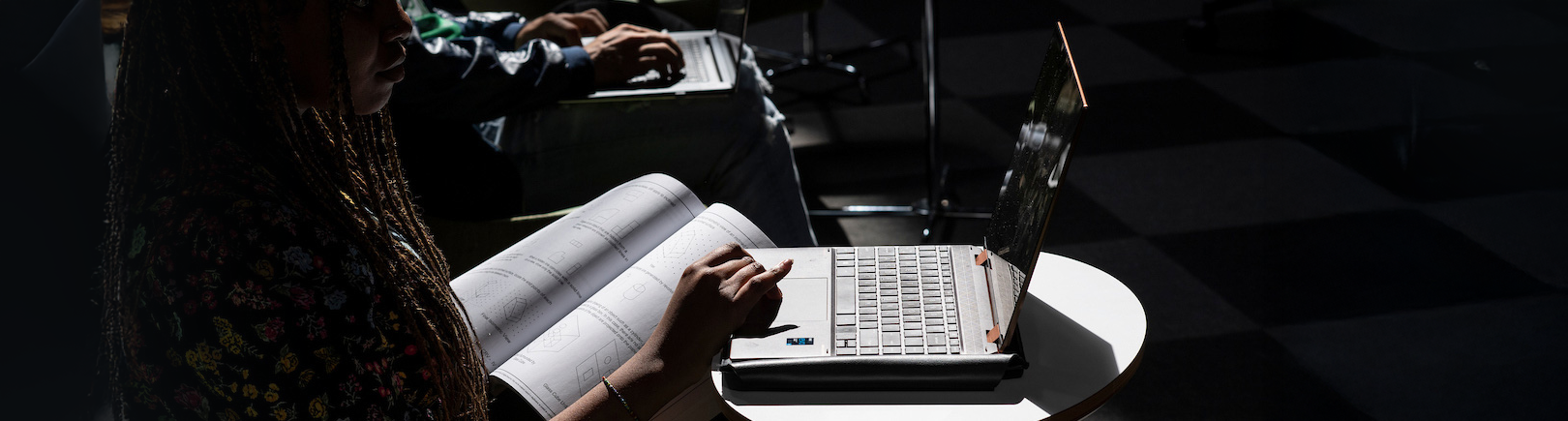 Top horizontal photo banner of students working on laptops and textbooks in a dimly lit study area.