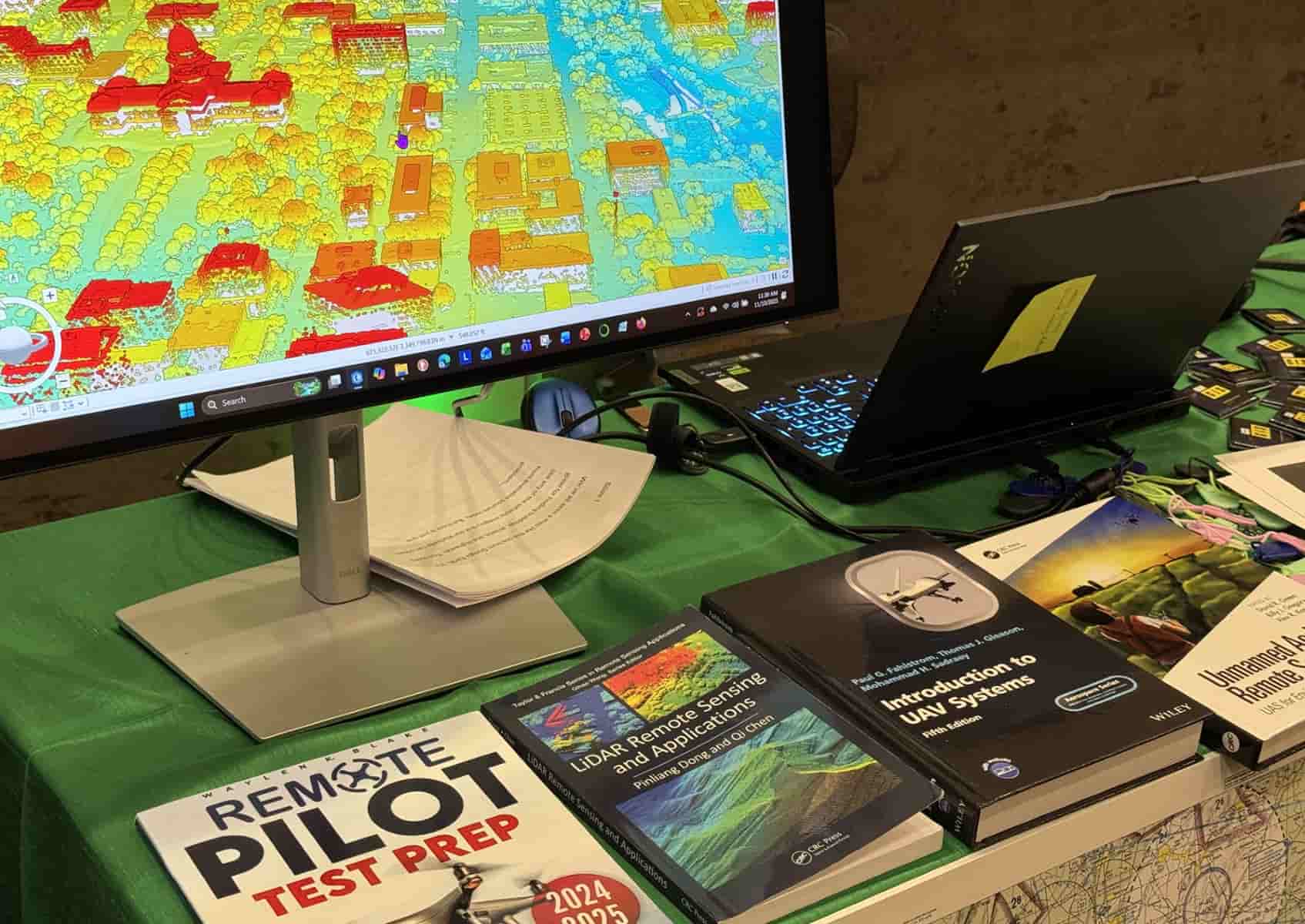 Photo of a computer monitor displays colorful LIDAR imagery. Below the screen is a row of books on remote piloting and drones.