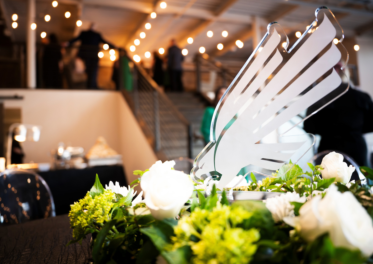 Photo of UNT's Salute to Faculty Excellence awards celebration venue of a table covered with white flowers and a variety of greenery around a crystal sculpture of the diving eagle logo symbol.