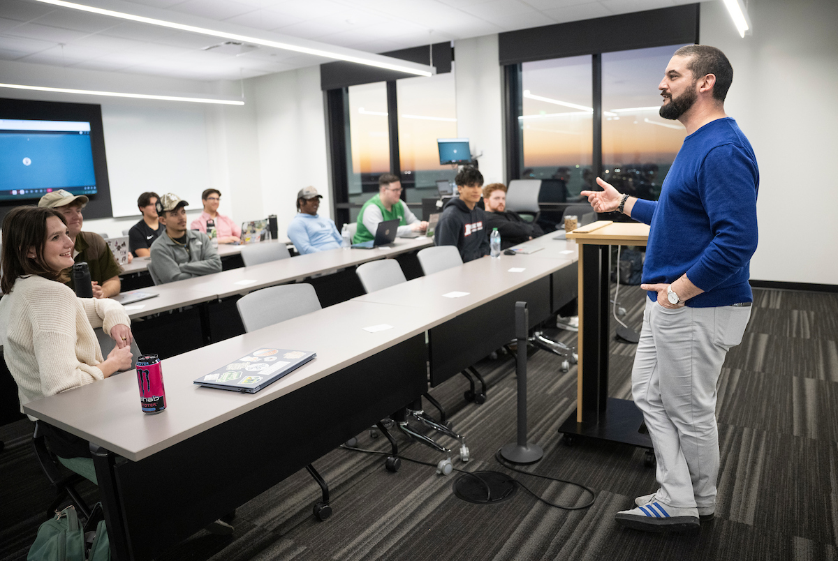 Joe Trahan addressing a group of UNT at Fresco's students in a classroom. Photo of Joe Trahan addressing an engaged group of students in a modern classroom with a sunset skyline visible through the windows.