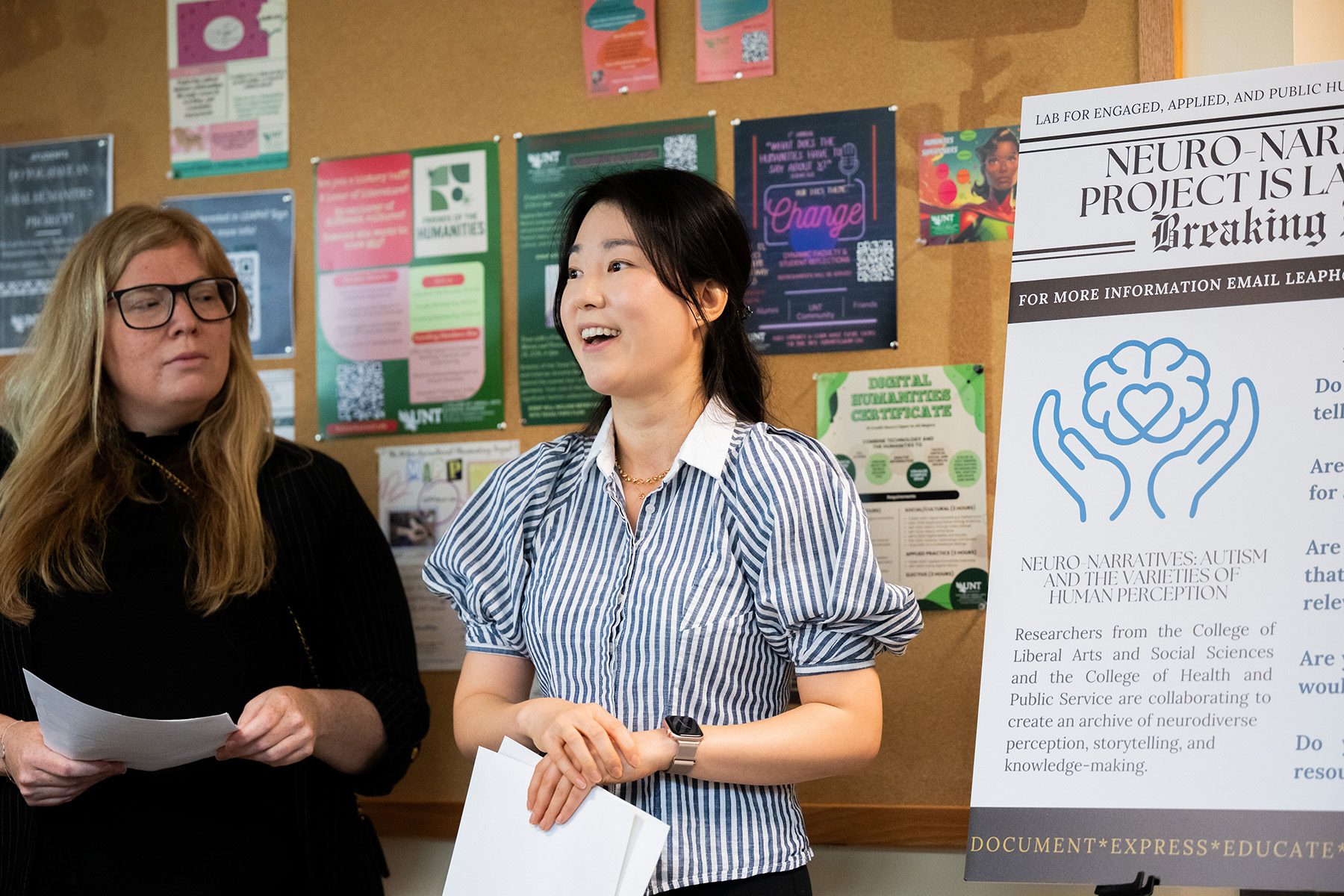 A photo of two UNT faculty stand next to a posterboard with information about a neuro-narratives project