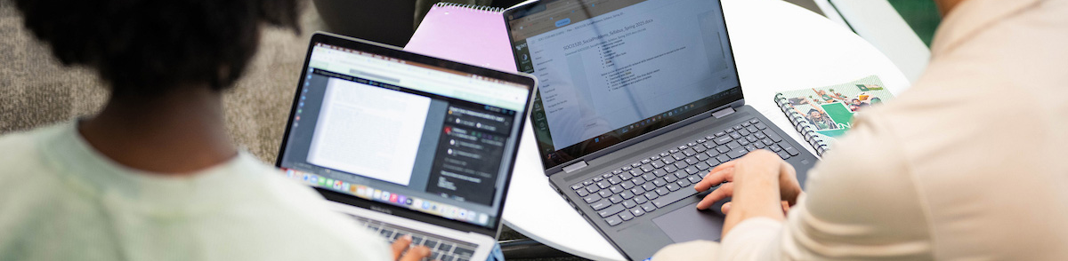 Photo banner of UNT two UNT students work on their laptops at a table, focusing on their screens. Top horizontal, narrow-cropped photo banner of two UNT students work on their laptops at a table, focusing on their screens.