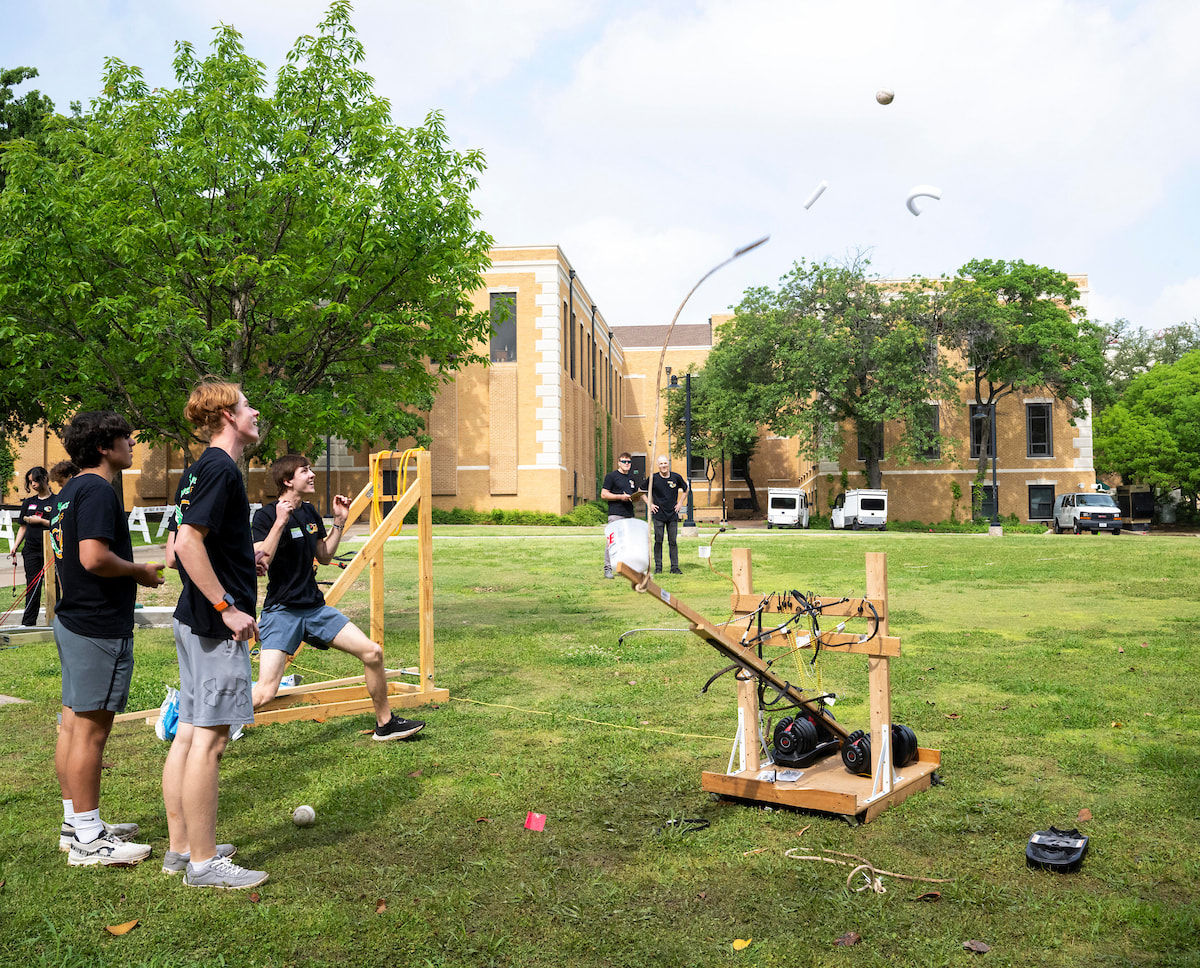 Photo of student cheers after a catapult launch, two others watch at UNT