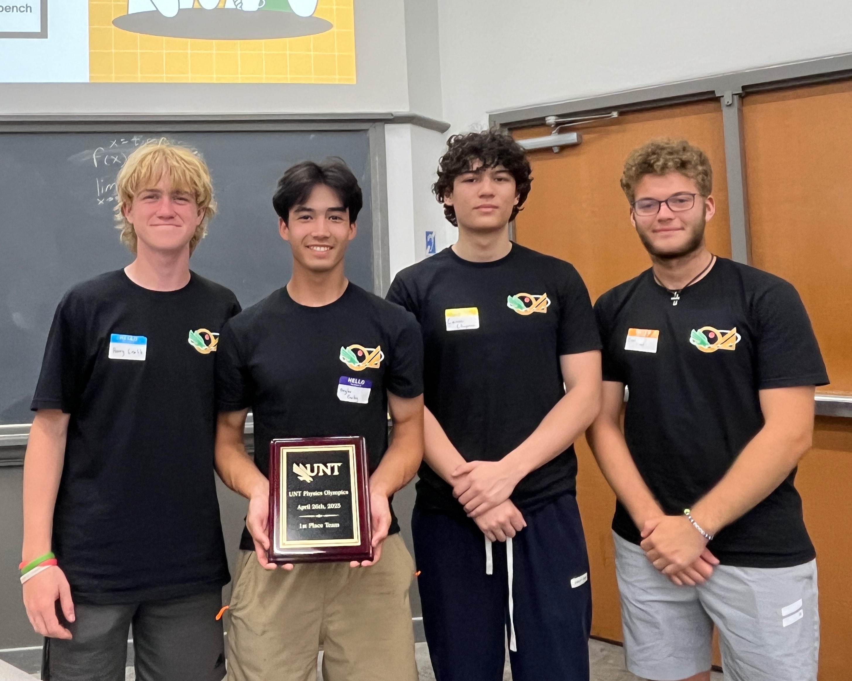 Photo of four students as they hold their first place plaque from the UNT Physics Olympics