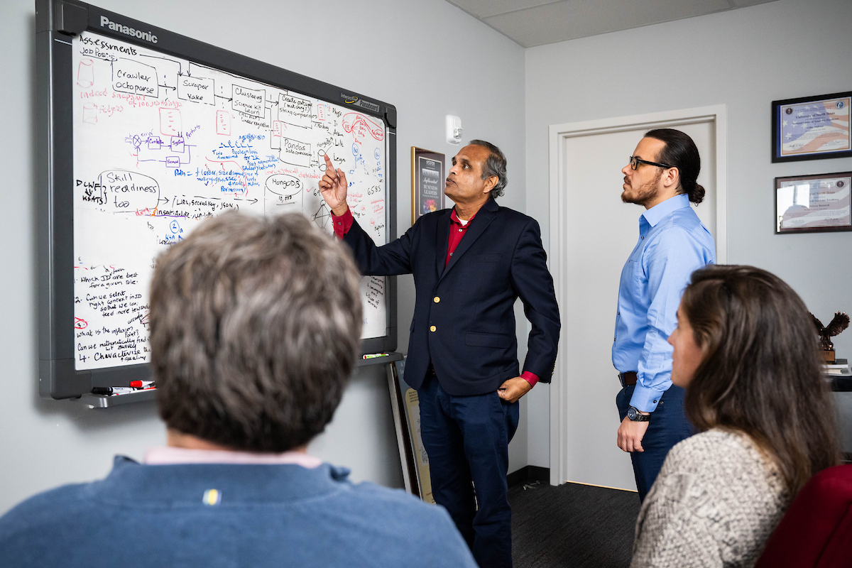UNT's Dr. Ram Dantu his students as they discuss ideas in front of a whiteboard filled with diagrams and notes. Photo of UNT's Dr. Ram Dantu his students as they discuss ideas in front of a whiteboard filled with diagrams and notes.