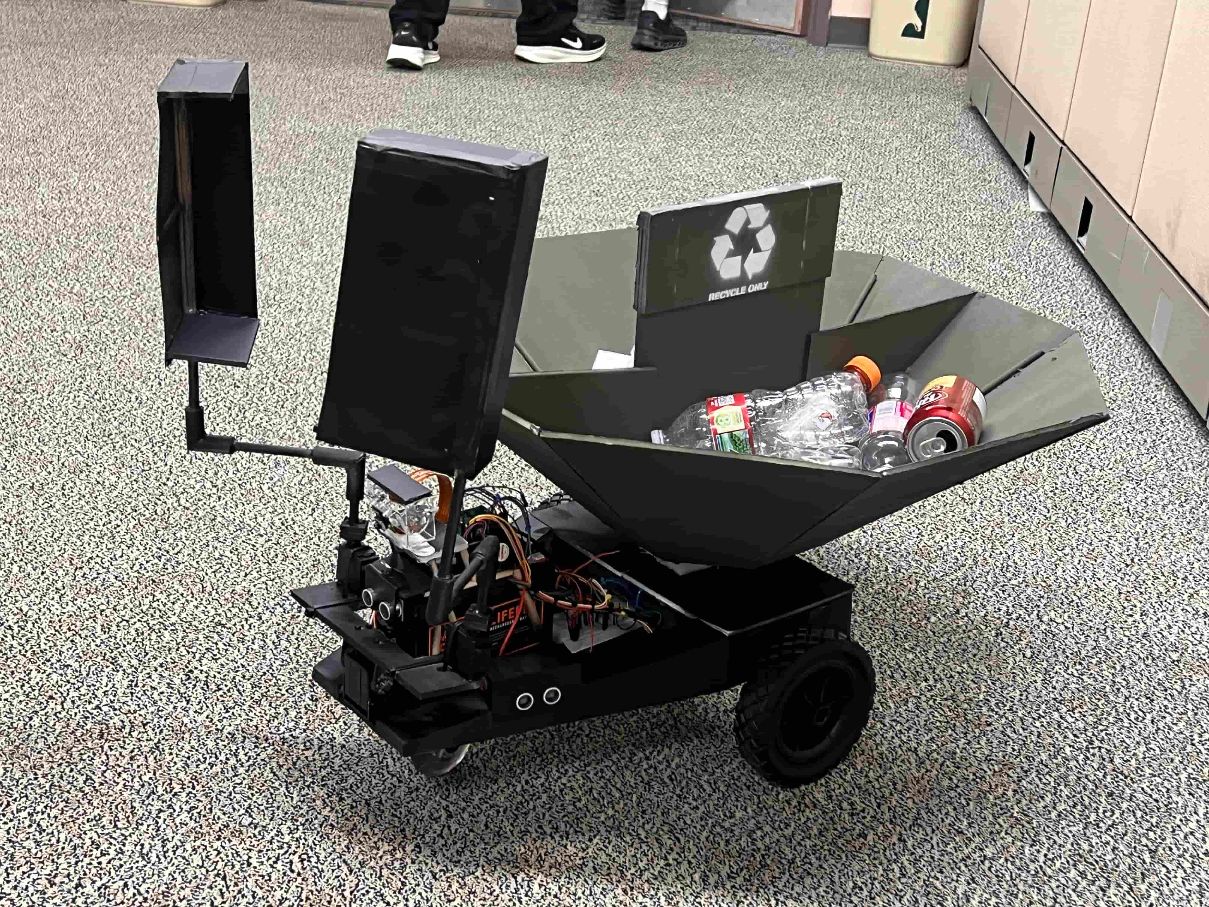 A photo of wheeled motorized robot platform with two scoopers attached to the front and a basket in the back for collecting trash