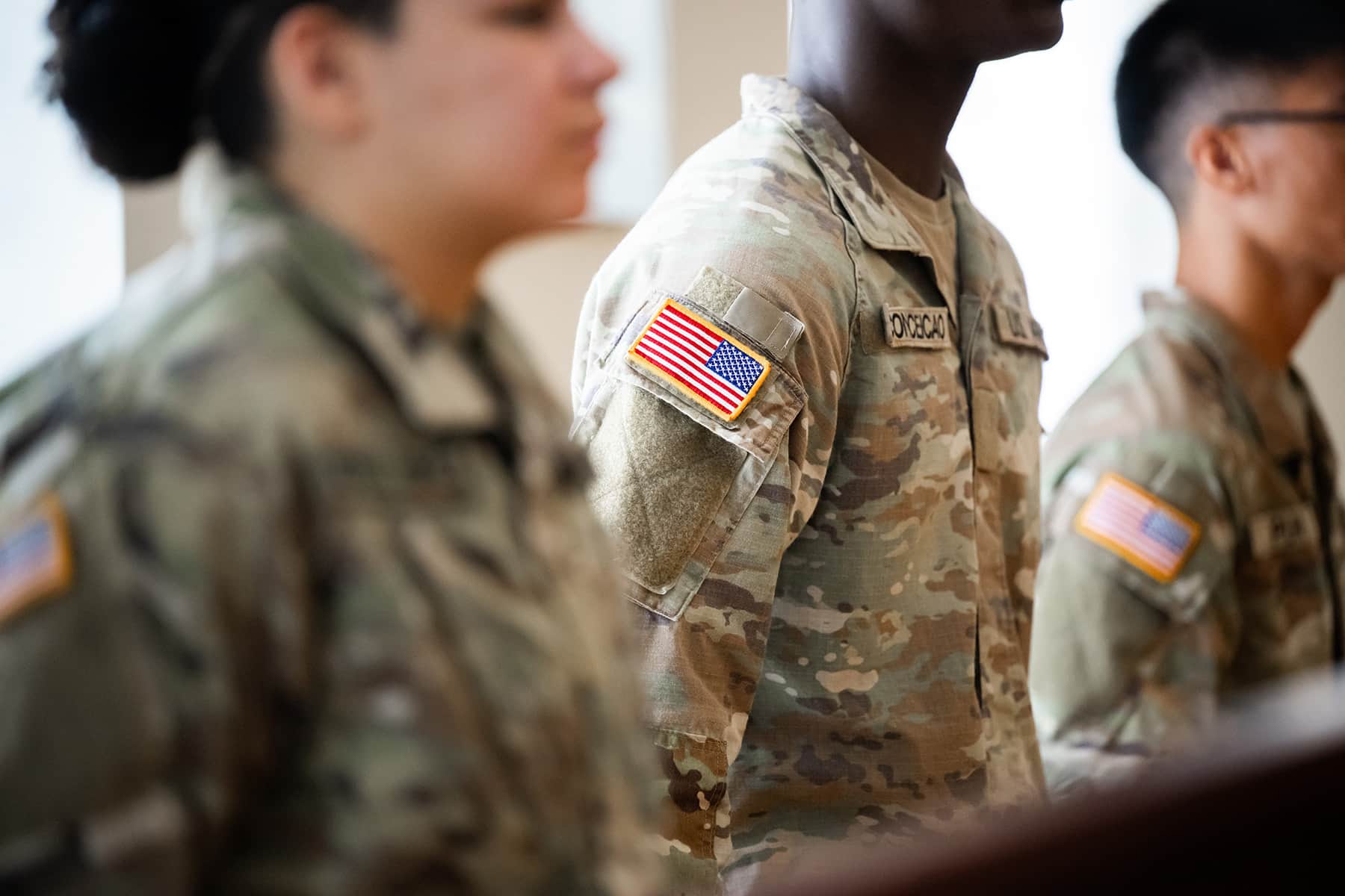 A close-up image of three UNT DFW U.S. Army ROTC cadets in uniform standing in formation. The photo's selective focus is on the shoulder patch of the US flag.