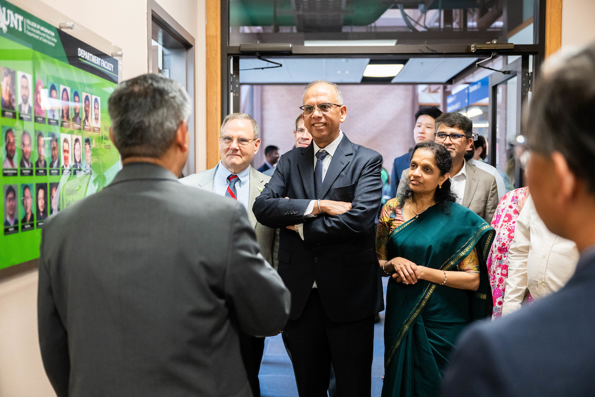 Photo of the Sinha with a group in a UNT school room speaking to someone who's back is to the camera