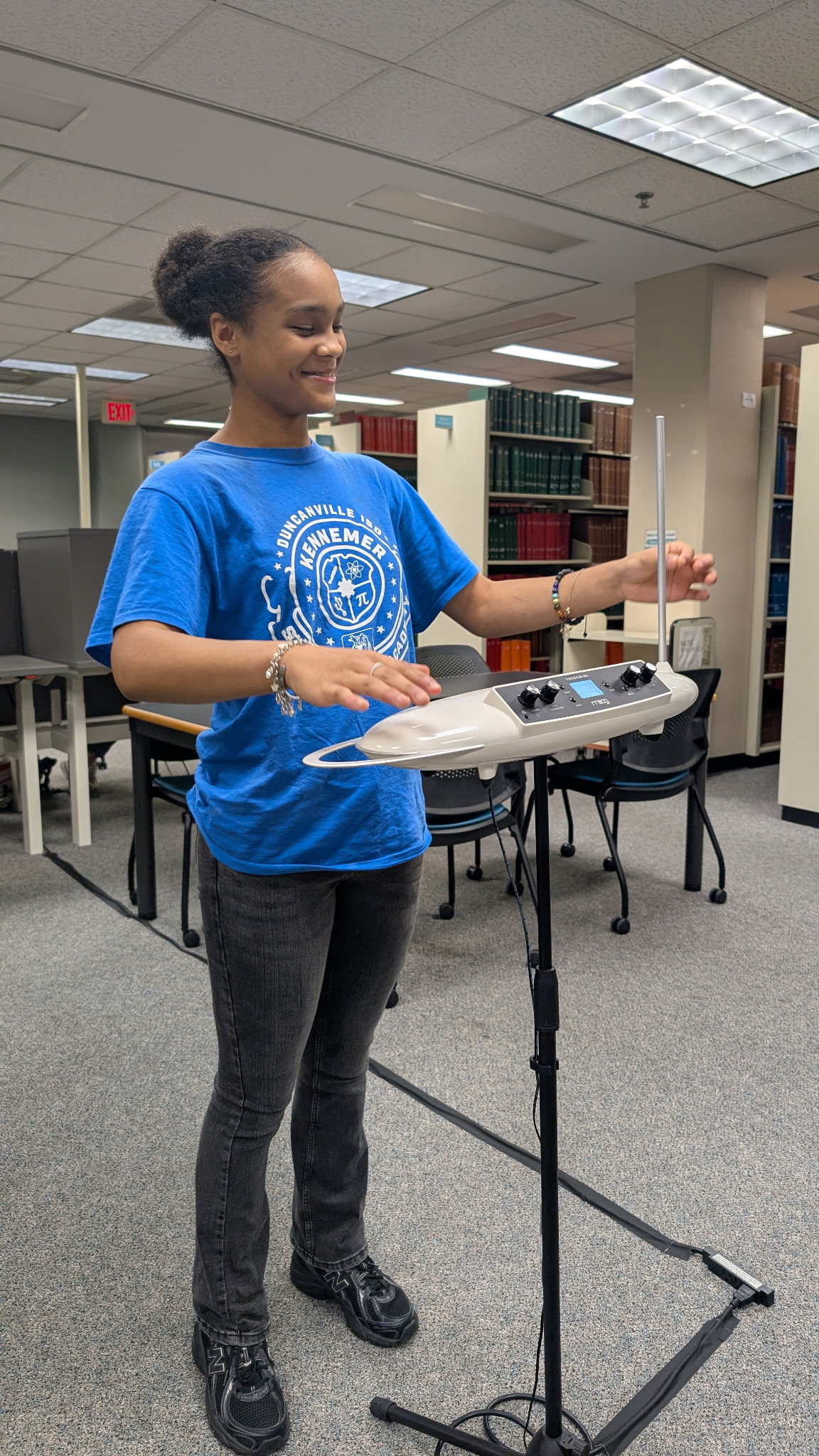 A female middle school student in a blue shirt waves her hand over a machine to make music Photo of a female middle school student in a blue shirt waves her hand over a machine to make music