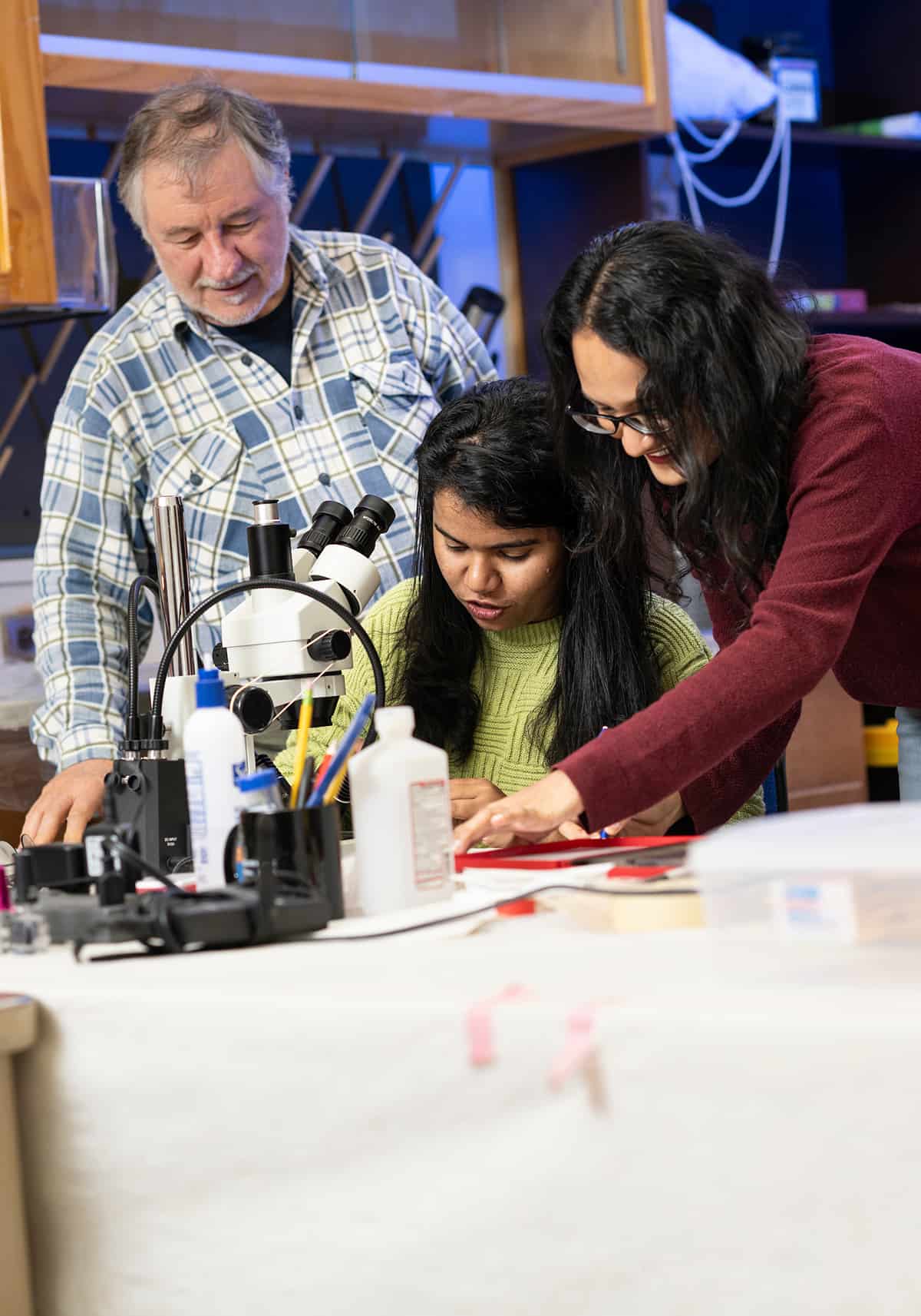 Photo of three UNT researchers study moss and lichen samples under a microscope