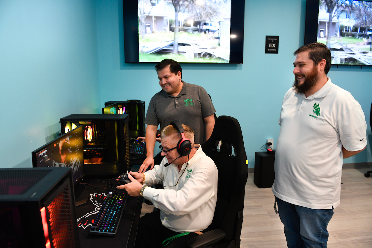 Photo of a man plays on a computer as two others looks on and laugh happily