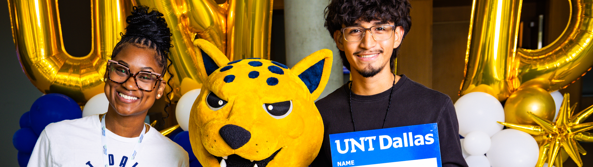 Top horizontal cropped banner photo of UNT Dallas UNT Dallas student and staff member pose with mascot Jax on the first day of class
