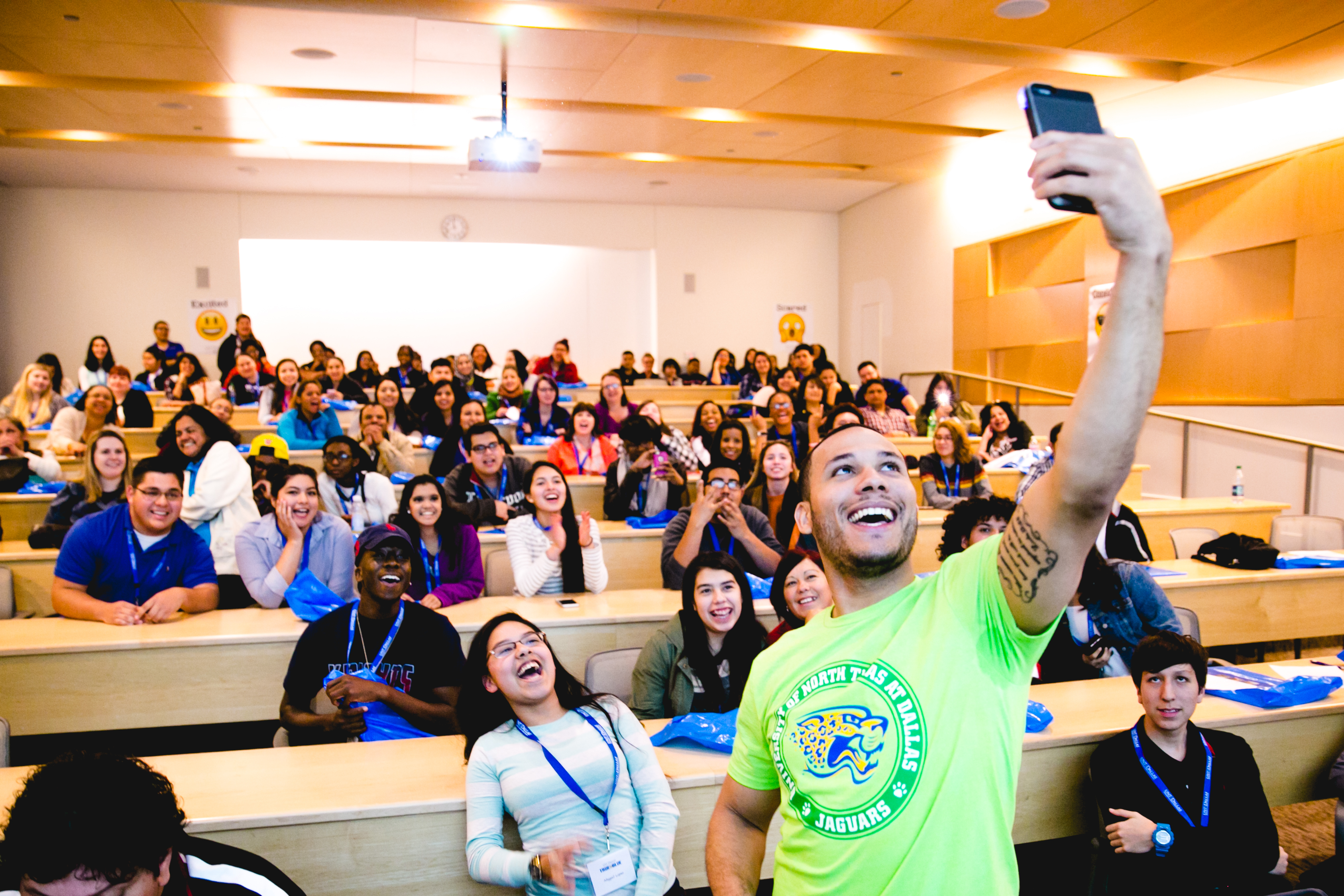 Photo of a UNT Dallas prospective student takes a selfie during a campus open house known as "True Blue" in a tiered classroom.