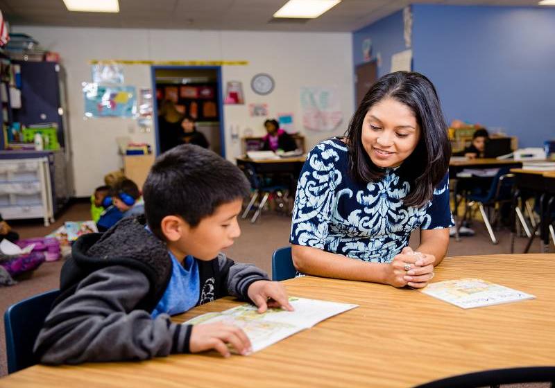 Photo with the foreground focus of UNT Dallas's graduate student working with a child in an elementary school classroom. 