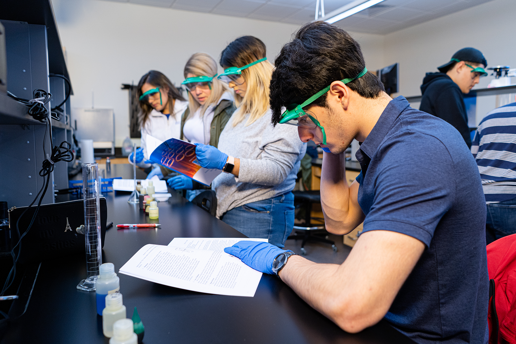 UNT Dallas Pre-health students in science lab at UNT Dallas Photo of UNT Dallas STEM students wearing safety goggles and blue gloves review lab instructions and examine materials during a chemistry class experiment.
