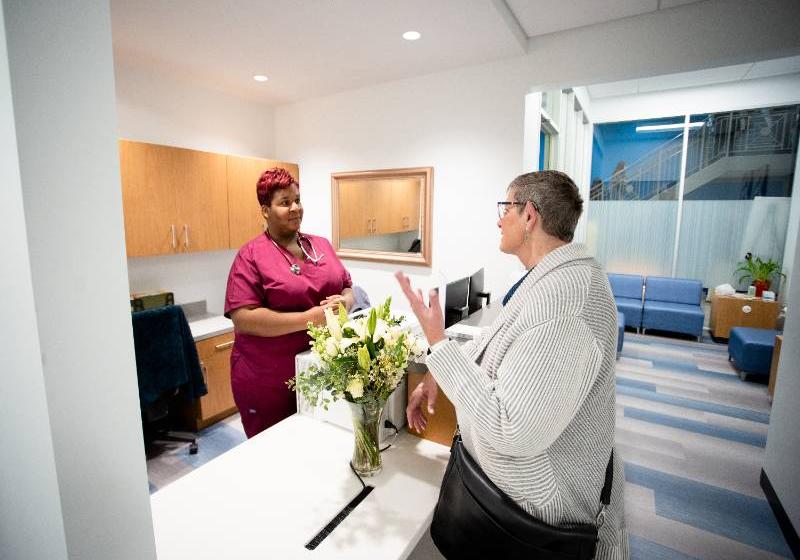 A photo of UNT Health's clinic at UNT Dallas. A woman is at the center talking with on of the employee's wearing magenta scrubs.