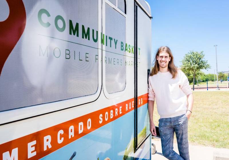 Photo of UNT Dallas's public health alumni Hunter Marion is standing next to a mobile farmers market community refrigerated food truck.