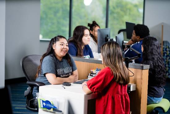 Photo of a UNT Dallas student meeting with an advisor. The picture uses selective focus on them. Behind them are two other advisors wit students that are out of focus.