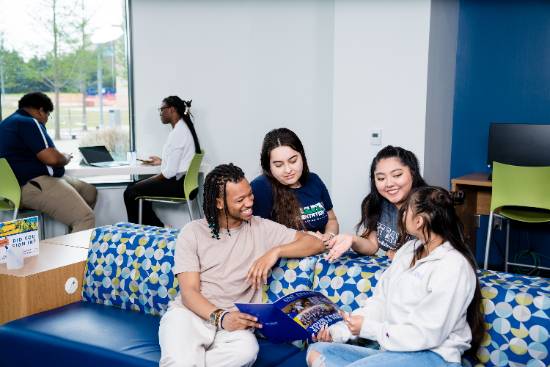 Photo of a group of ethnicity diverse male and female UNT students together, two are siting on a couch and two other's are behind them