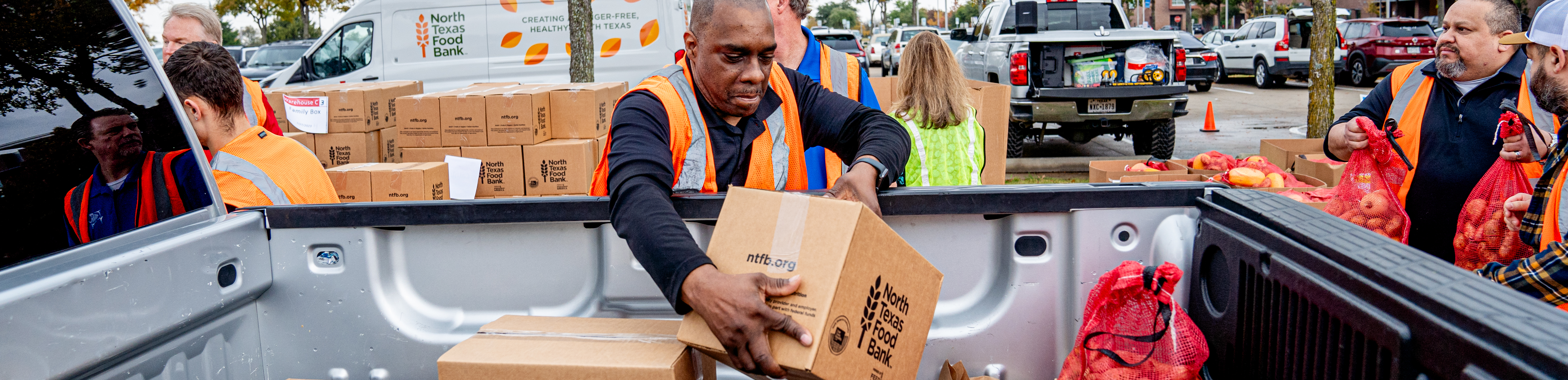 Picture of the top banner shows volunteers loading boxes and bags of food into the back of a pickup truck during a food distribution event. The boxes are labeled "North Texas Food Bank," and the volunteers are wearing safety vests. A van in the background also displays the North Texas Food Bank logo