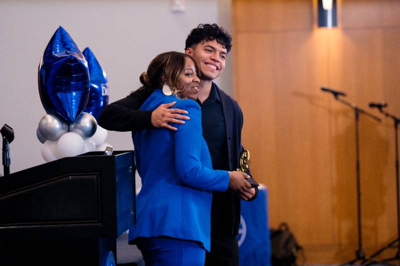 Photo of Trailblazer Elite (TBE) scholar Sergio Barrera hugs program director Dr. Kimberly Riddick at the TBE 5th Anniversary Celebration