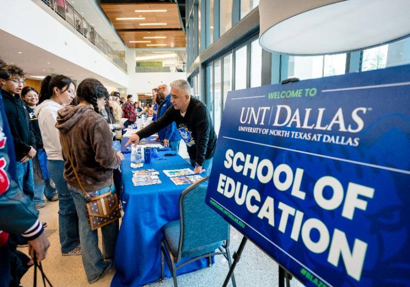 A photo of students visit the UNT Dallas School of Education table at an indoor university event.