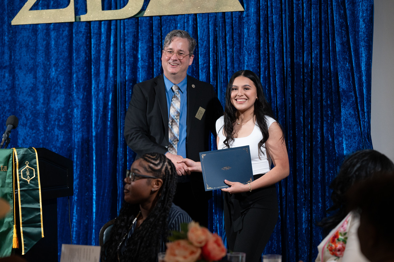 Photo of UNT Dallas's School of Business Dean, Dr. Jason Garrett, presents an award to a smiling student at the school's Annual Spring Gala