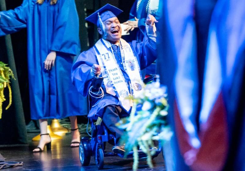 Photo of a graduate in a wheelchair smiles with pride and joy as his name is called during commencement 