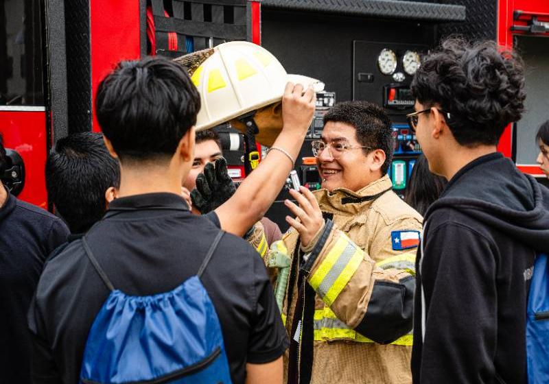 A high school student tries on a firefighter's helmet and gear as classmates watch Photo of ahigh school student tries on a firefighter's helmet and gear as classmates watch