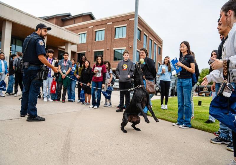 A four-legged officer interacts with students as his two-legged partner holds onto the leash Photo of a four-legged officer interacts with students as his two-legged partner holds onto the leash