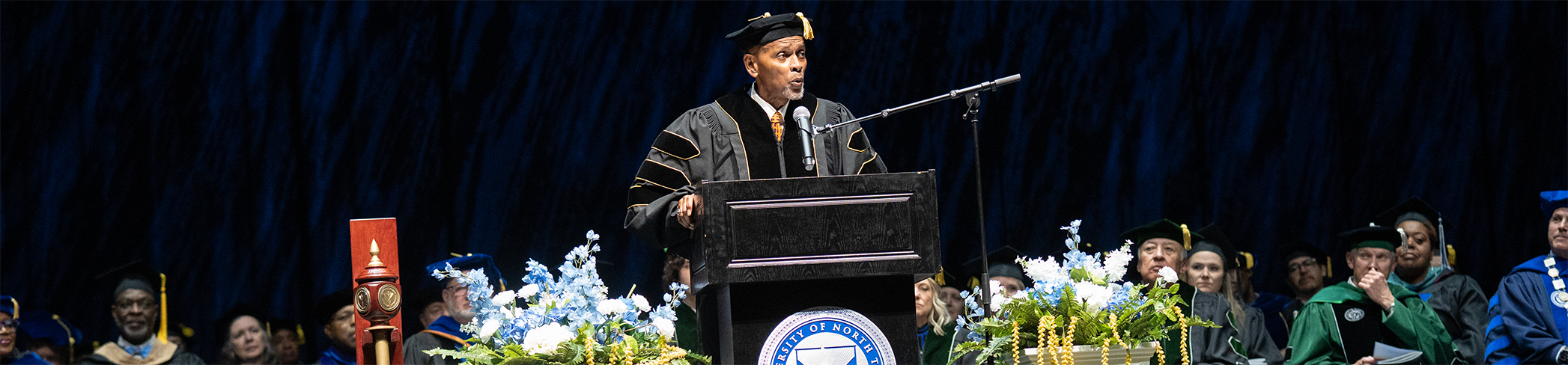 banner photo of Roland Glynn Parrish in academic regalia speaking at a podium during the UNT Dallas 2026 Spring Commencement graduation ceremony. Top horizontal cropped banner photo of Roland Glynn Parrish in academic regalia speaking at a podium during the UNT Dallas 2026 Spring Commencement graduation ceremony.
