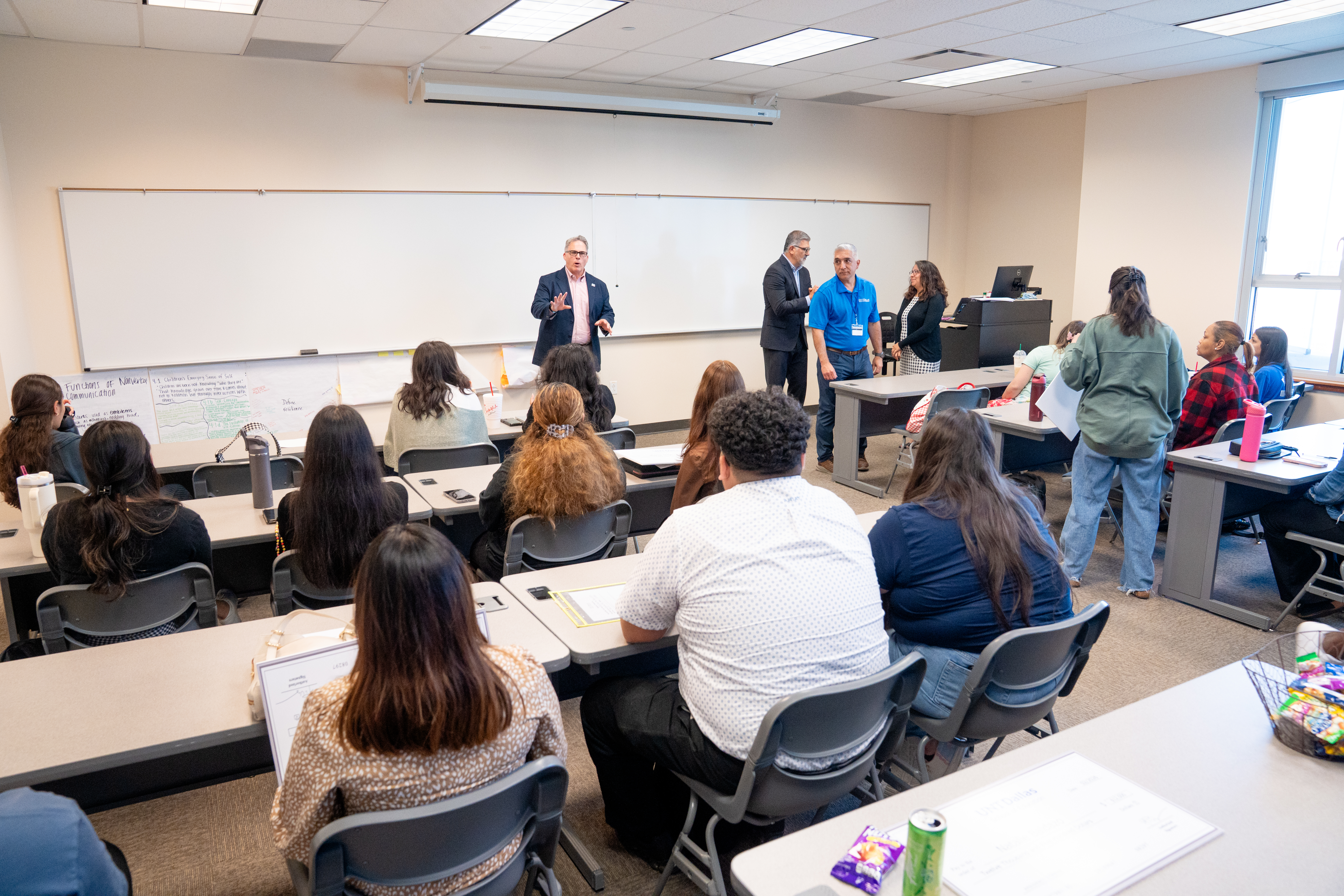Students in the UNT Dallas Teacher Residency Program listen as President Warren von Eschenbach celebrates their success and commitment, as Interim Dean Dr. Patrick Valdez, Administrative Coordinator David Casarez and Director of Clinical Practice Emily Waneck listen nearby. Photo of inside a classroom with UNT Dallas students in the UNT Dallas Teacher Residency Program listen as President Warren von Eschenbach celebrates their success and commitment, as Interim Dean Dr. Patrick Valdez, Administrative Coordinator David Casarez and Director of Clinical Practice Emily Waneck stand nearby to the side.