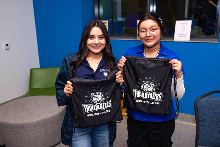 A photo of two new female UNT Dallas Trailblazers show their school spirit as they each hold dark blue with white branded t-shirts at 2025 NSO 