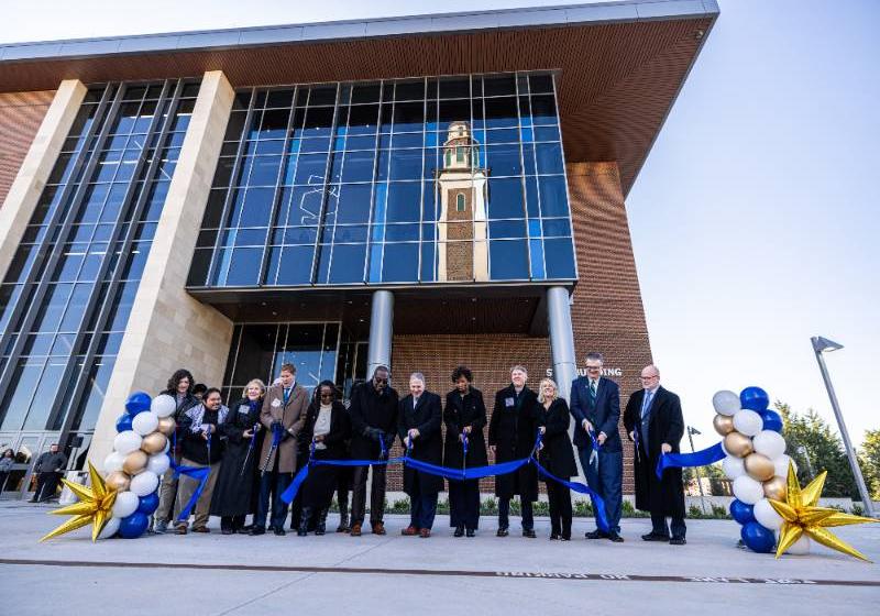 Photo of The University of North Texas at Dallas leaders and other dignitaries cut the ribbon to celebrate the new STEM Building. Reflected in the windows is the Ryan Tower.