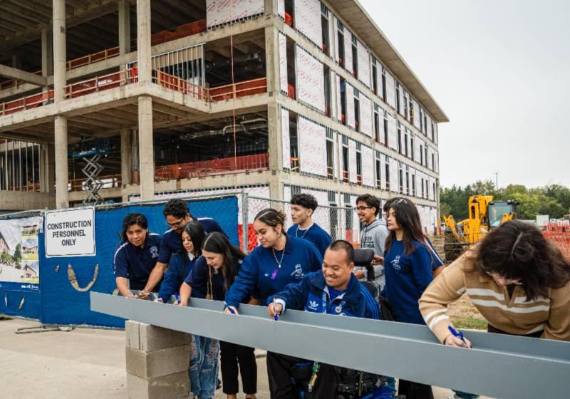 Photo of students sign the final steel beam for the topping off ceremony of the UNT Dallas STEM Building, Opening in Dec. 2025 