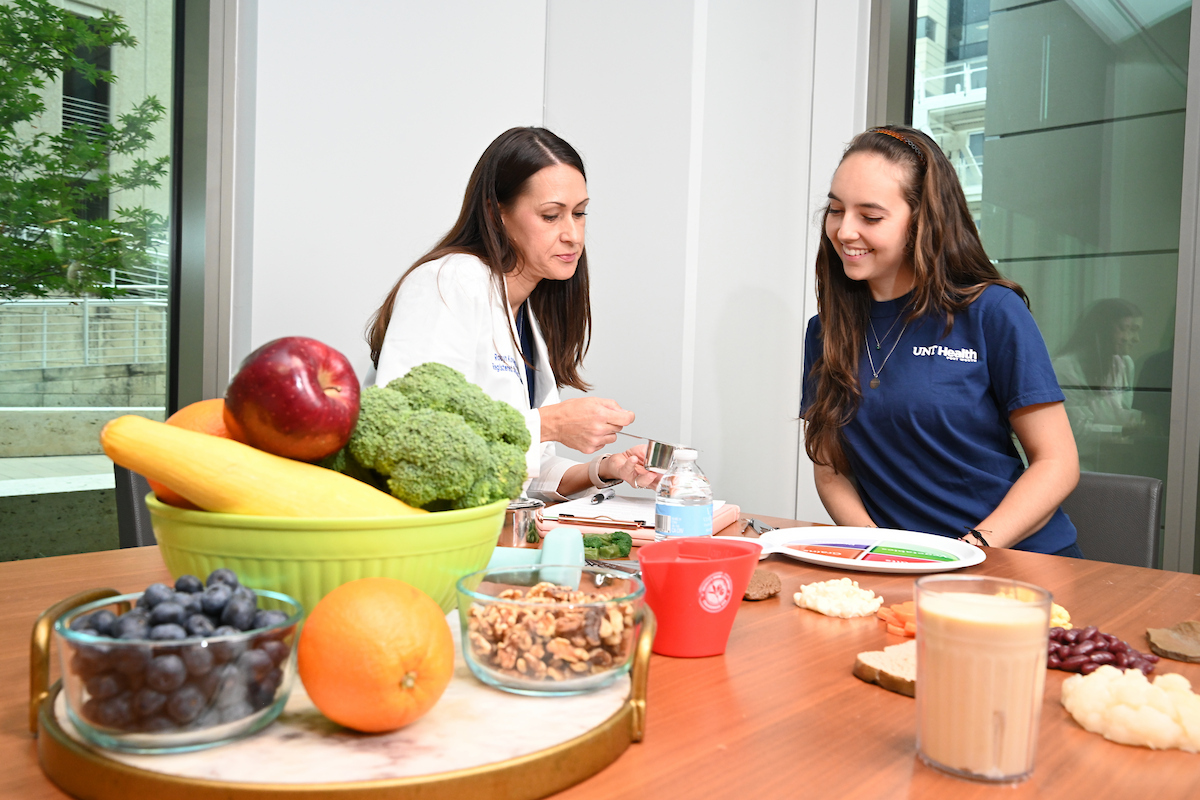 Photo of UNT Health nutritionist consulting with a young female student at a table with healthy foods and a portion plate
