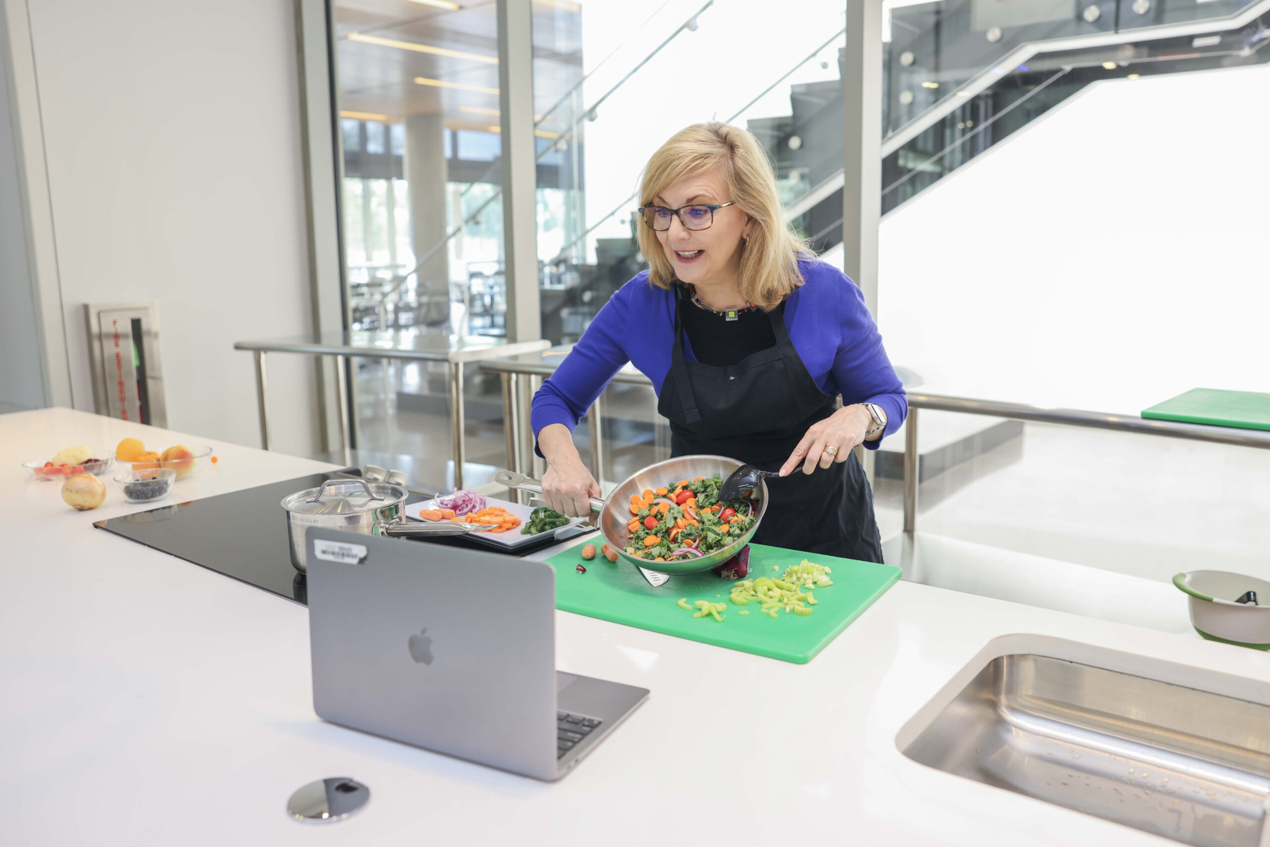Full photo of a woman in an apron at UNT Health is preparing a colorful vegetable dish during a virtual cooking session.