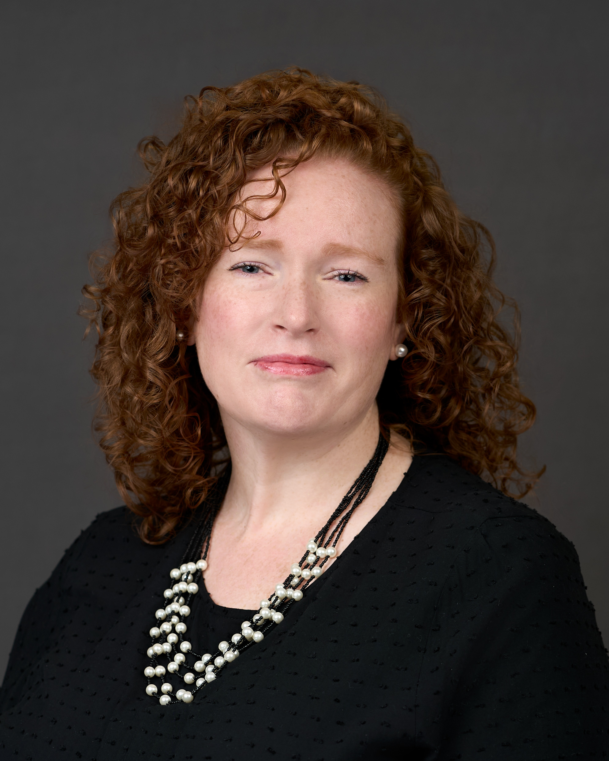 Photo portrait of UNT Health's Sarah Clark, a woman with red hair posing in front of gray backdrop.