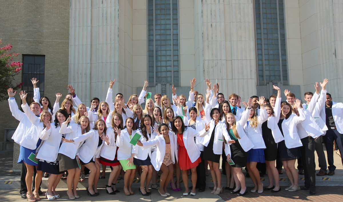 The full (uncropped) photo of a group of smiling UNT Health students wearing their white coats, posing and celebrating.