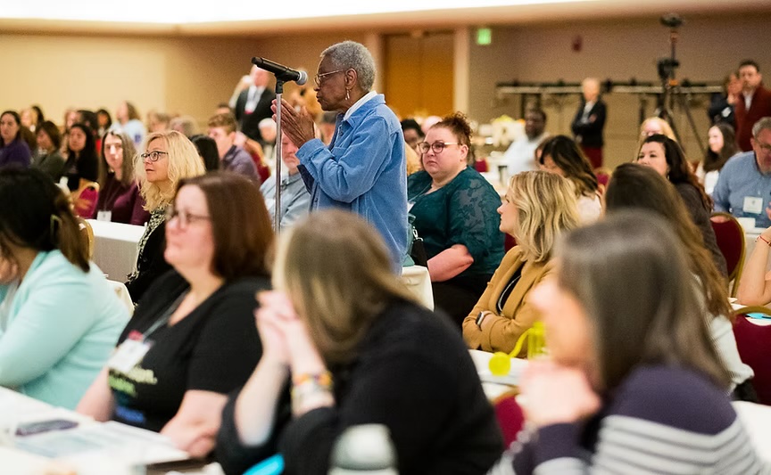 Photo of health professionals smiling and connecting during a previous Health Literacy Collaborative Summit networking session, speaking at a microphone stand.