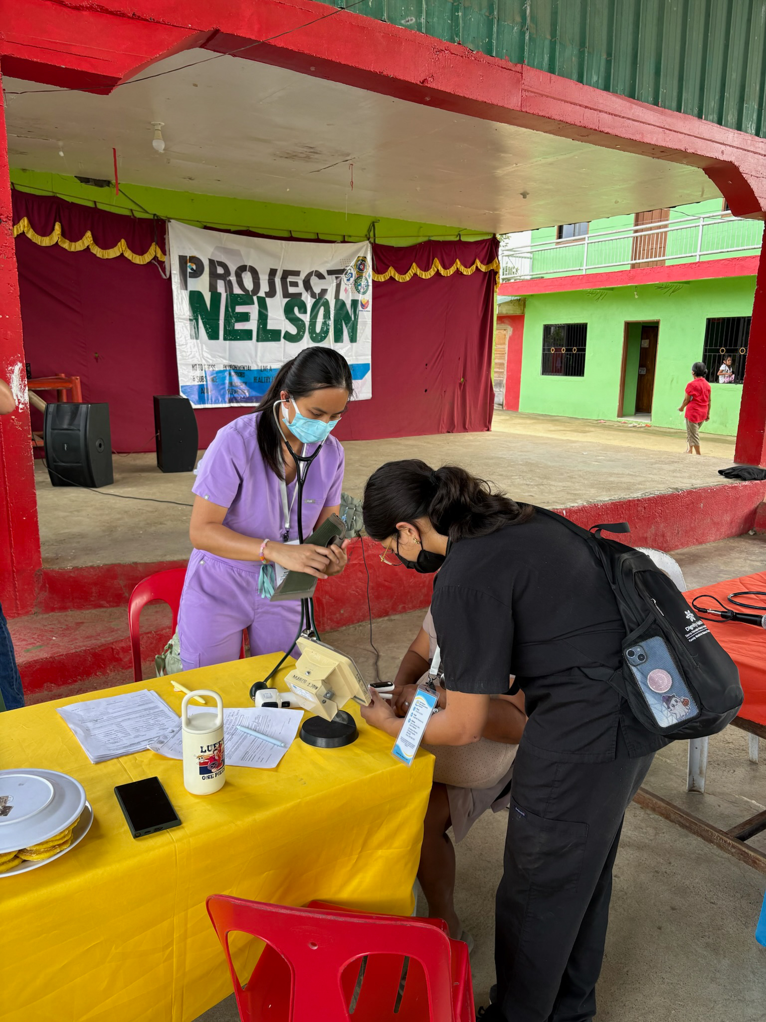Photo of UNT Health TCOM students conduct a patient health screening at an outdoor free clinic under a Project Nelson banner during the Bohol, Philippines medical outreach mission in January.