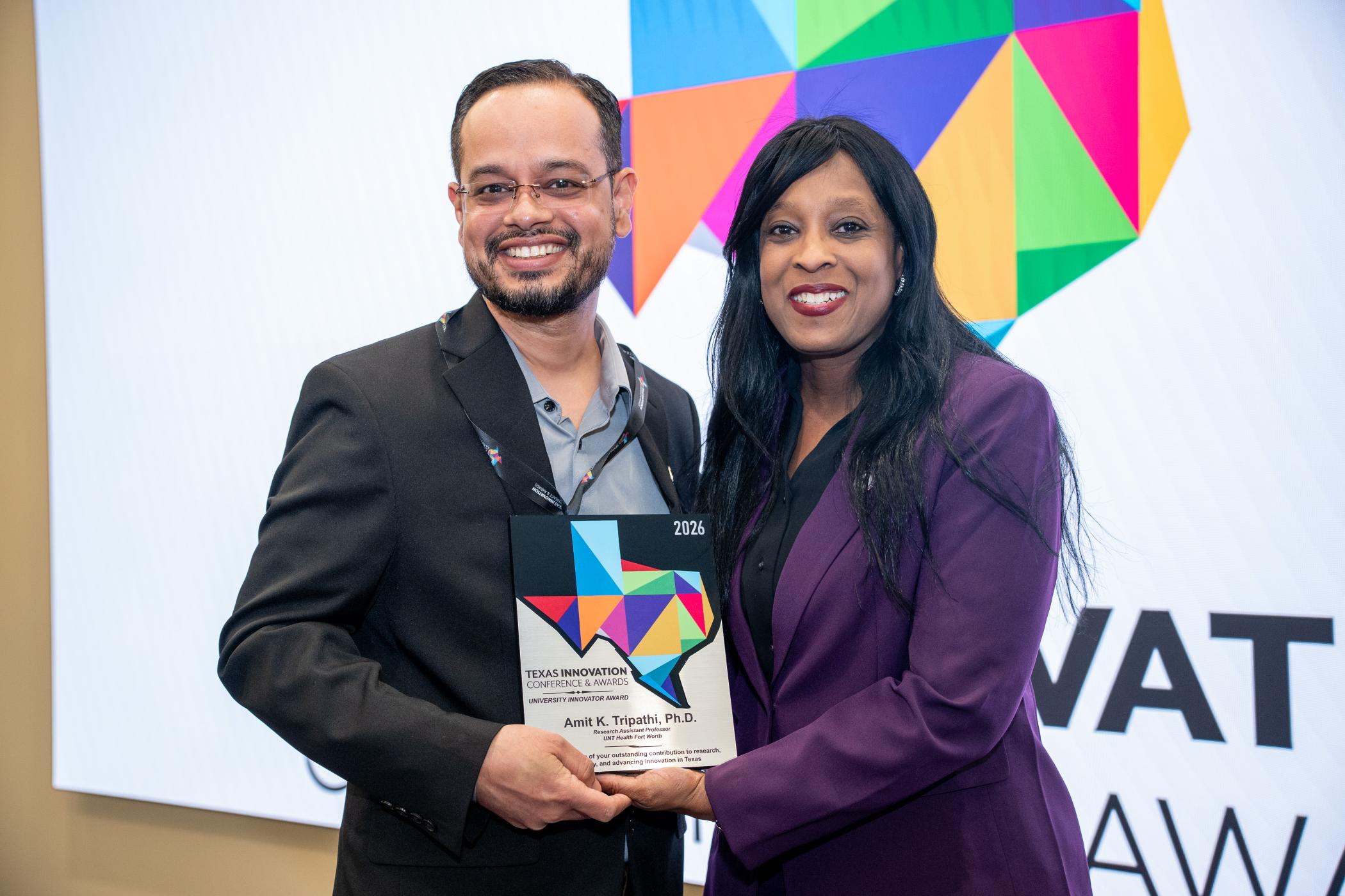 Photo of UNT Health's Dr. Amit K. Tripathi, Research Assistant Professor at UNT Health Fort Worth, receives his 2026 University Innovator Award plaque at the Texas Innovation Conference & Awards ceremony, posing alongside a presenter in front of the colorful event logo backdrop.